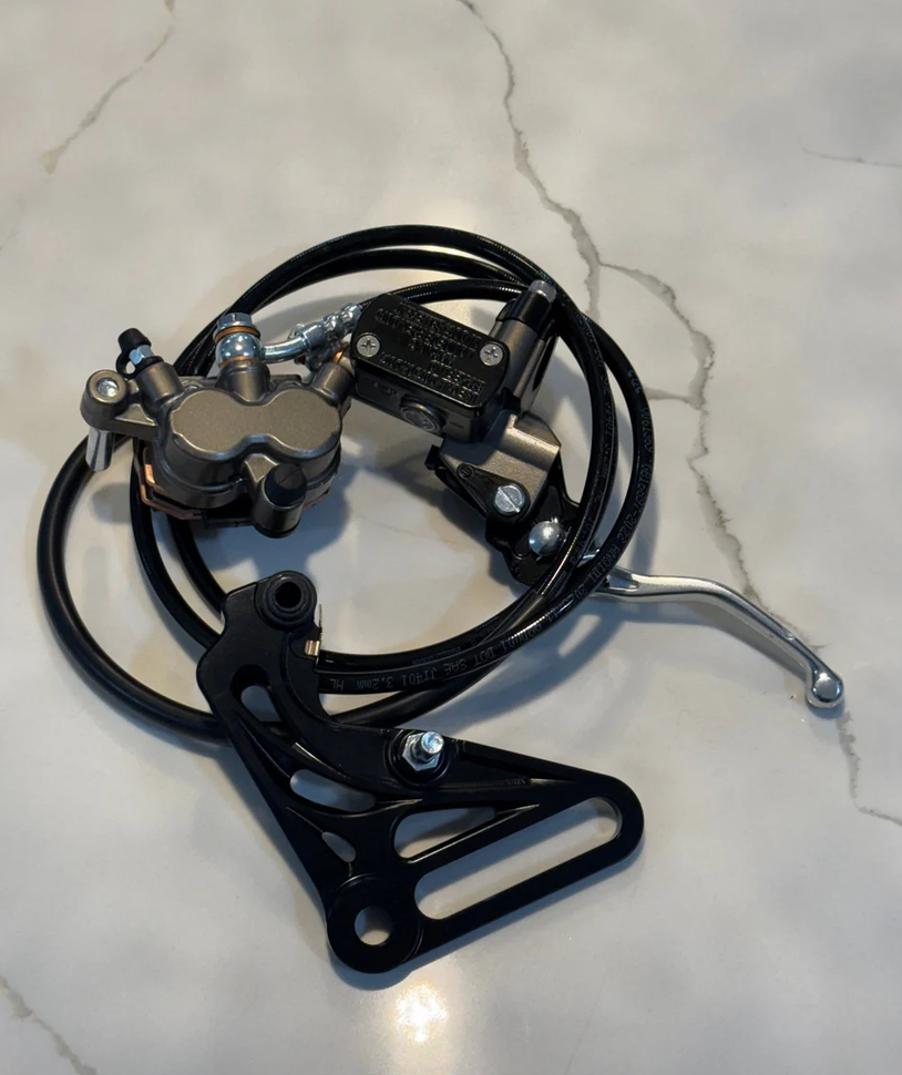 Tuttio Yozma brake kit components including brake caliper, hose, and mounting plate on a marble surface.